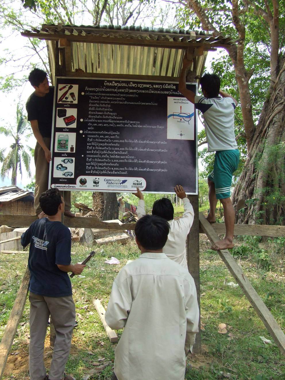 COMFISH staff work with villagers from Ban Muong Muan to nail down a sign board explaining village regulations.
